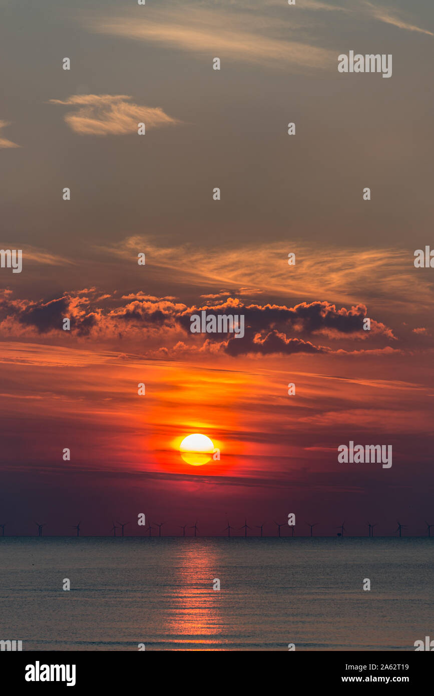 Rosso arancione tramonto con bellissimo Cielo e nubi e i mulini a vento sulla banda di orizzonte riflettendo sul mare Foto Stock