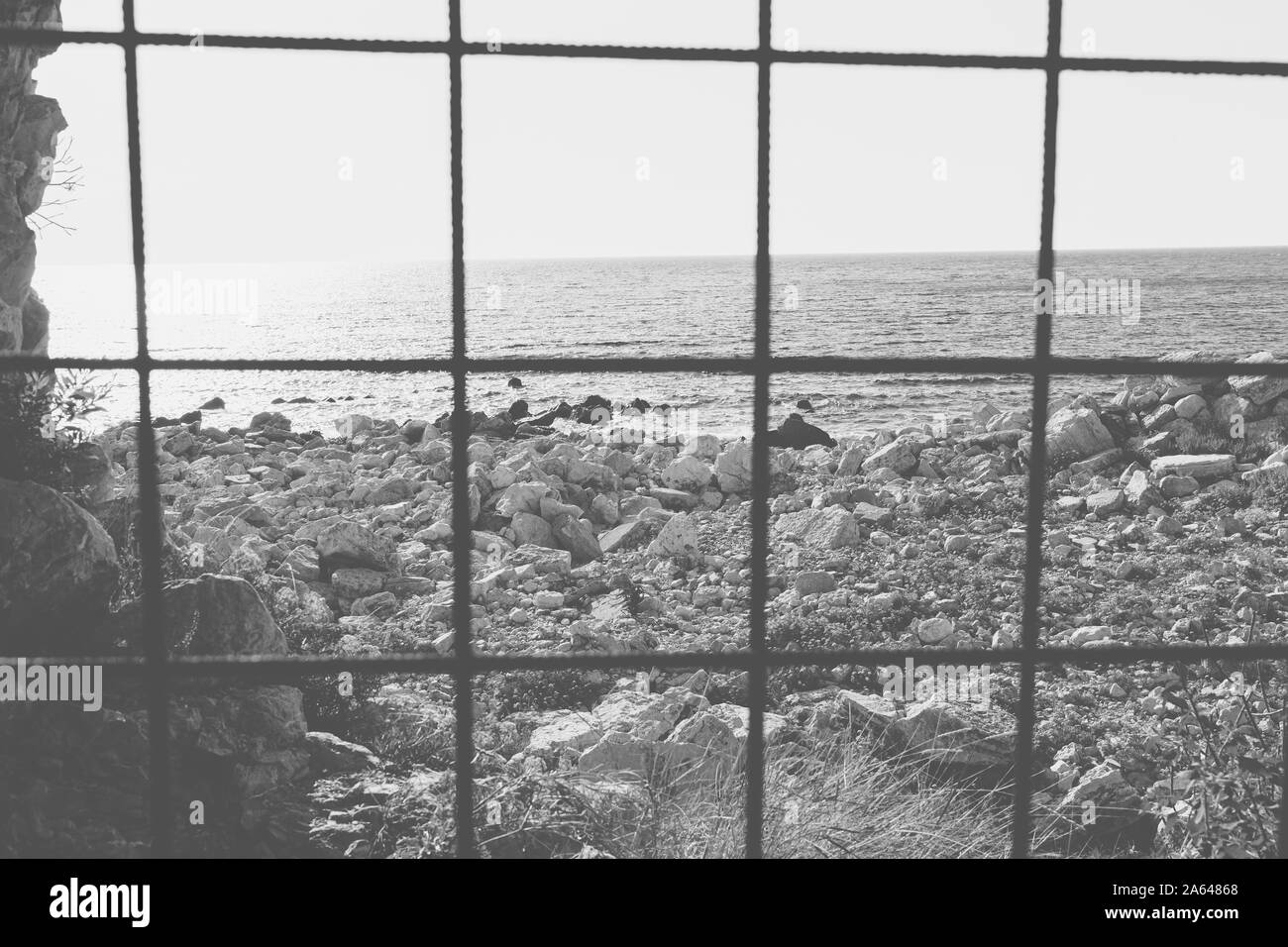La griglia di ferro con soleggiato mare e rocce sfondo, libertà concetto, immagine in bianco e nero Foto Stock