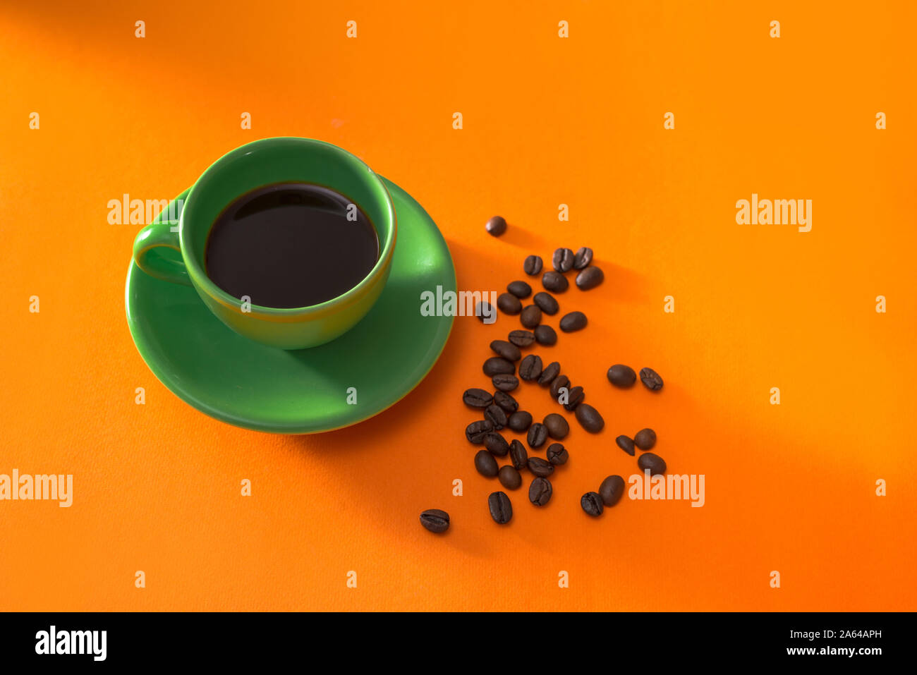 Green tazza di caffè con caffè torrefatto in grani su sfondo arancione Foto Stock