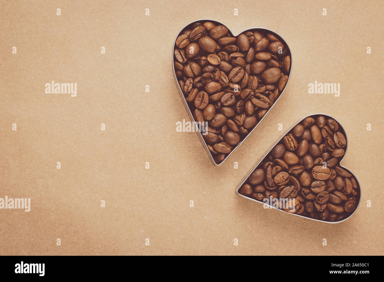 Cumulo di chicchi di caffè tostati. Due cuori di chicchi di caffè su sfondo neutro. Mockup, layout con il testo nello spazio. Marrone Vintage pergamena. Forma di ascoltare Foto Stock