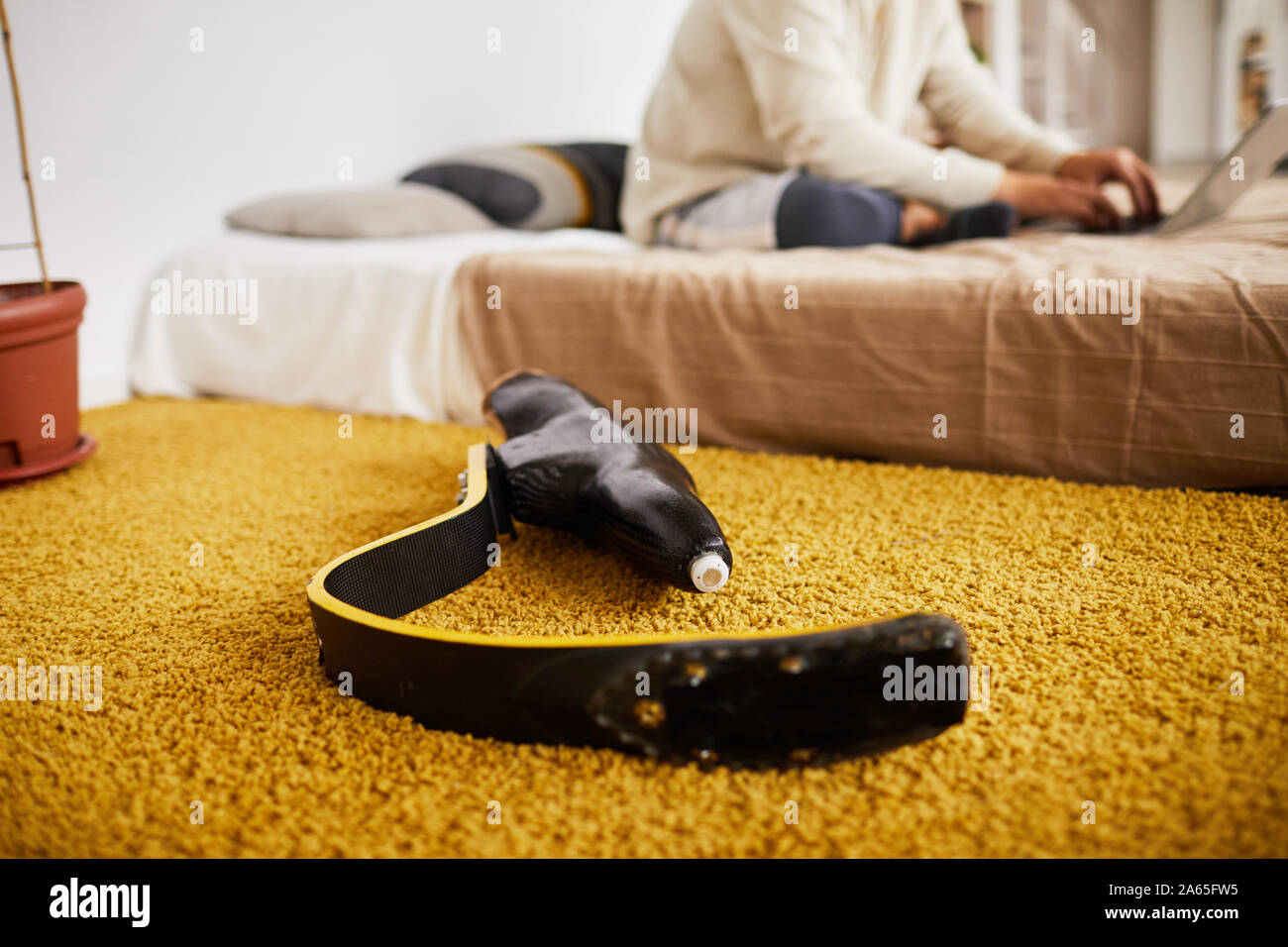 Close-up di protesi per gamba giacente sul tappeto con uomo seduto sul letto in background in camera da letto Foto Stock