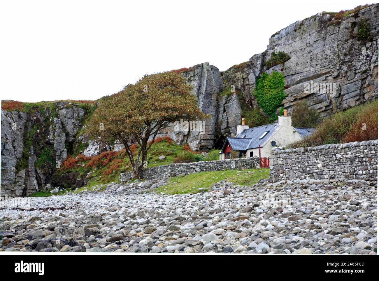 Una proprietà sul retro di una spiaggia sassosa sotto una scogliera rocciosa a Elgol, Isola di Skye in Scozia, Regno Unito, Europa. Foto Stock