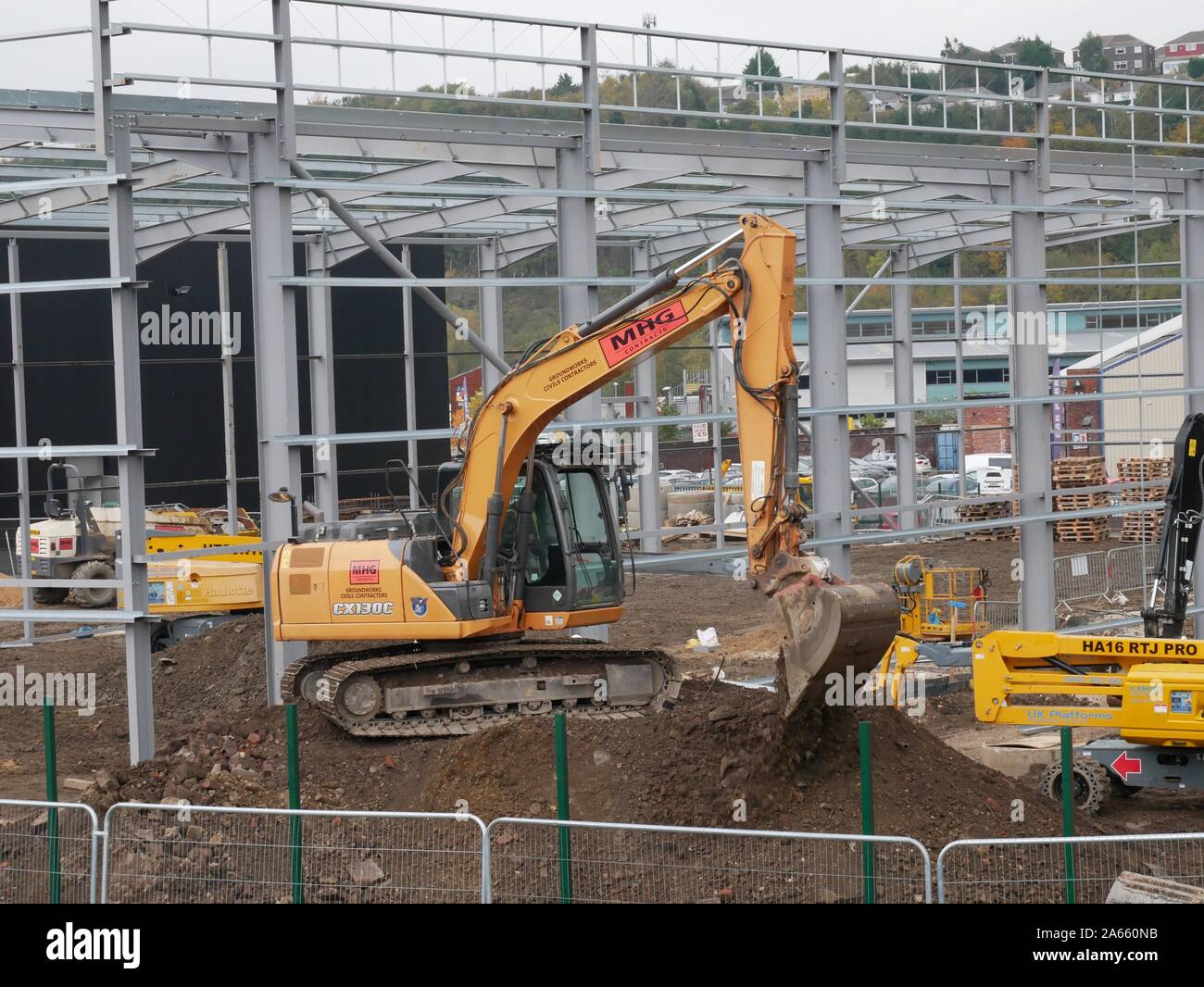 Un giallo di lavoro di scavo su un sito di costruzione con altre apparecchiature e il telaio di metallo costruzione essendo state edificate in Huddersfield nello Yorkshire Inghilterra Foto Stock