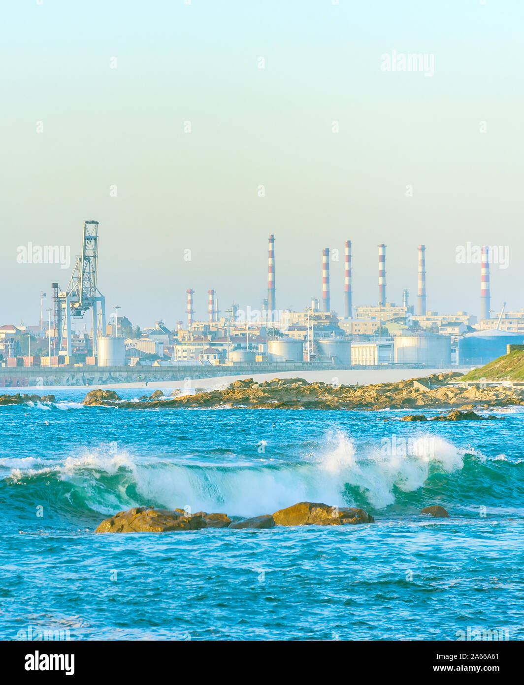 Tubi di impianti industriali sulla riva del mare, attrezzature portuali, nolo gru, onde brеaking on shore in presenza di luce solare, Porto, Portogallo Foto Stock