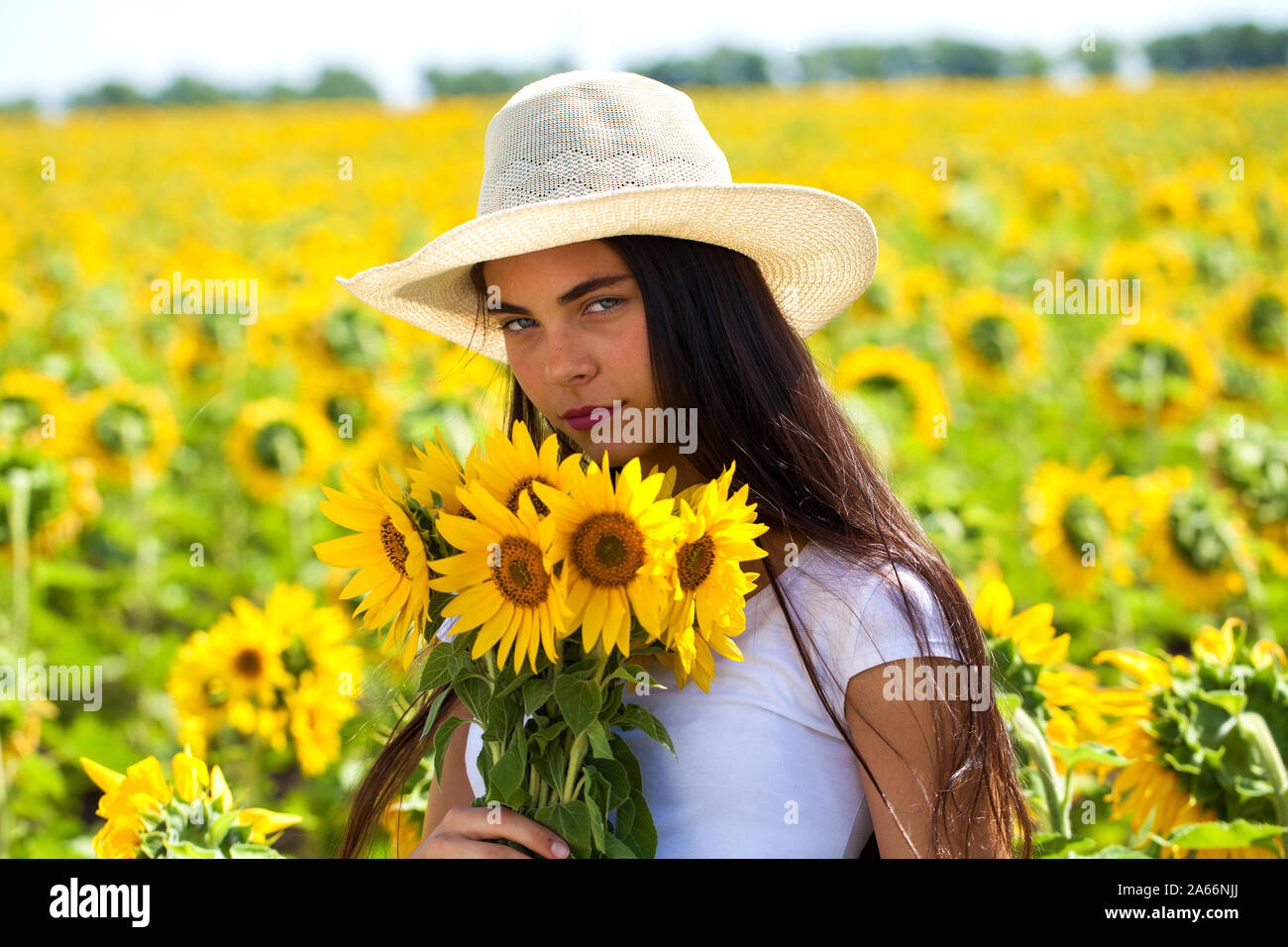 Ritratto di una giovane ragazza bella in un cappello di paglia e con un bouquet di fiori in un campo di girasoli Foto Stock