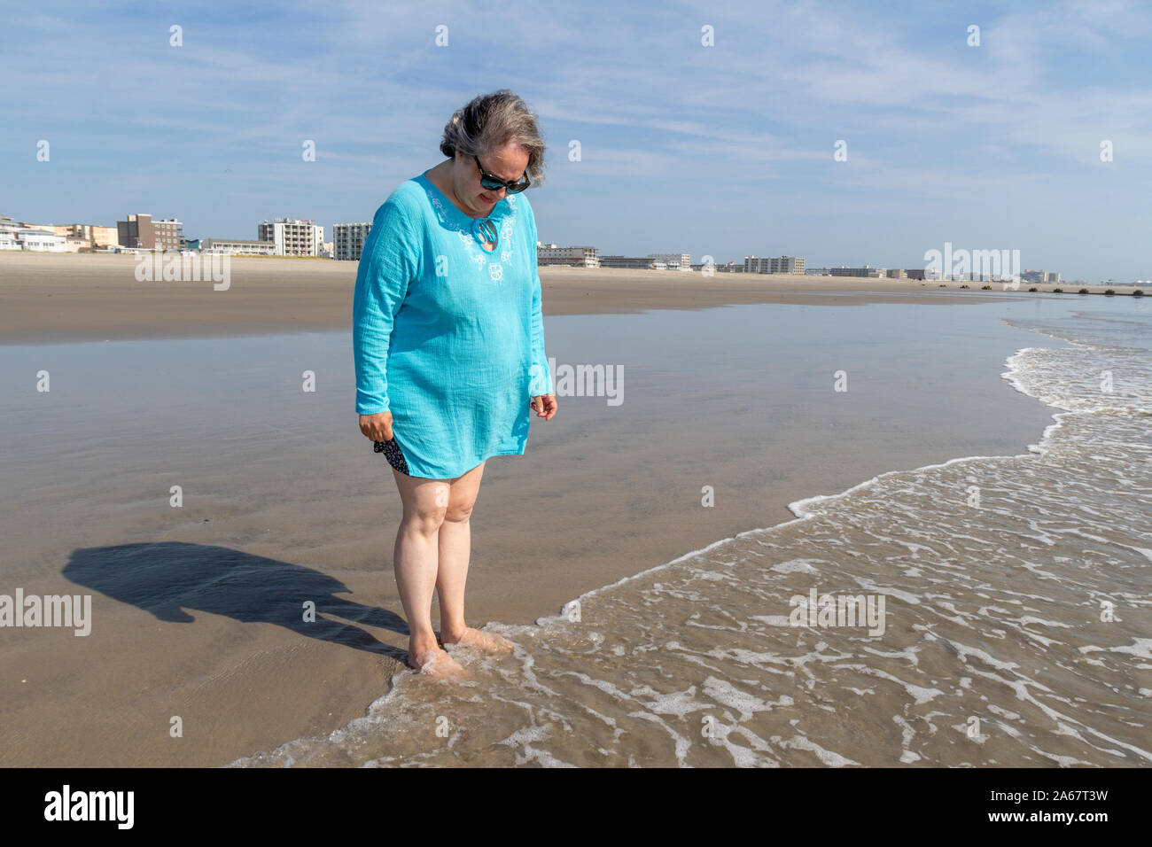 Un senior donna godendo di camminare nella sabbia sulla spiaggia dalla Ocean Shore. Foto Stock