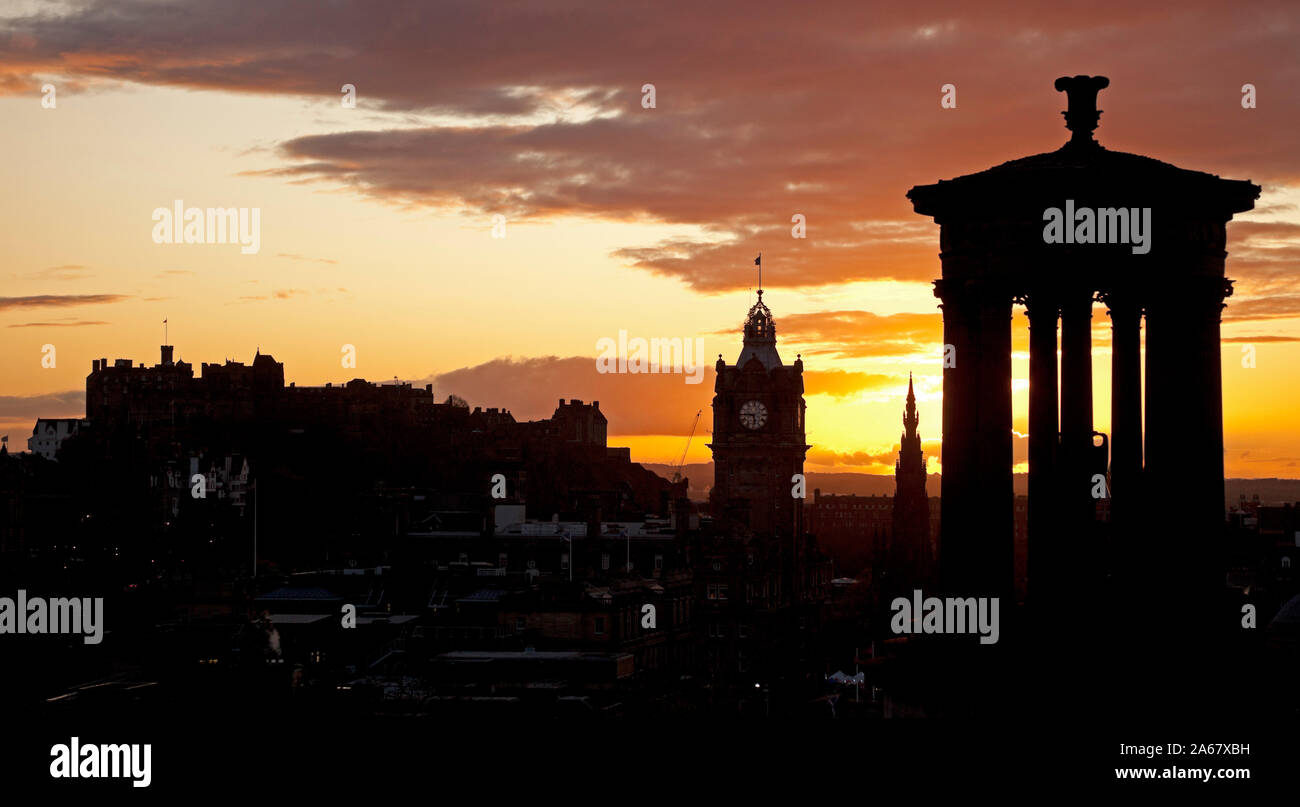 Calton Hill, Edimburgo, Scozia, Regno Unito. Il 24 ottobre 2019. Tramonto colorato sopra il centro della città dando una silhouette di Dugald Stewart monumento e il castello di Balmoral Hotel in centro. Foto Stock