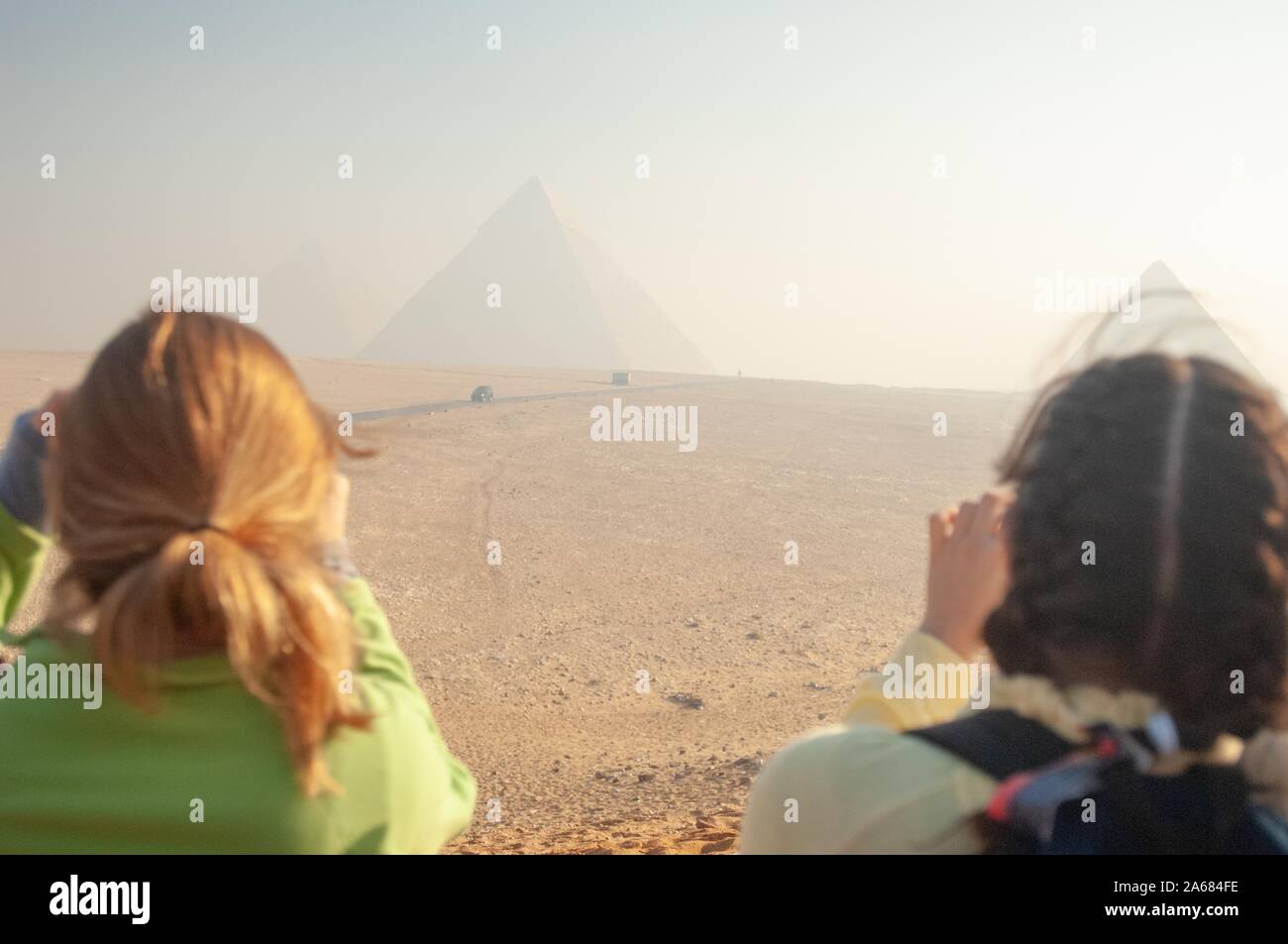 Oltre la spalla colpo di due Johns Hopkins University gli studenti al di fuori in una giornata di sole, scattare fotografie di una coppia di piramidi in distanza, di Giza in Egitto durante un programma di studio all'estero, 7 gennaio 2008. Dall'Homewood raccolta di fotografie. () Foto Stock