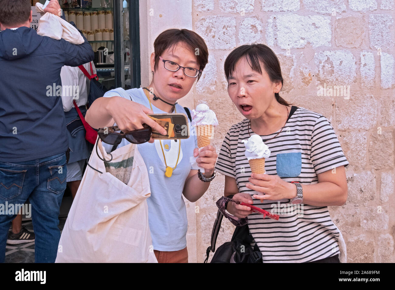 2 turisti provenienti da Taiwan prendere selfies di se stessi con gelato (gelato?) coni al di fuori di un negozio nella città vecchia di Dubrovnik, Croazia. Foto Stock