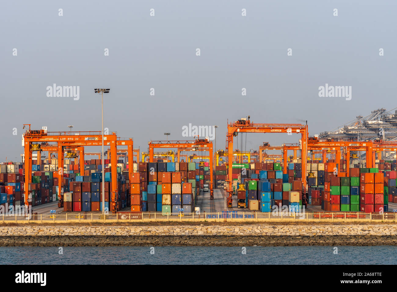 Il Porto di Laem Chabang seaport, Tailandia - 17 Marzo 2019: cerca attraverso pile di contenitori di spedizione sul quay con alti vettori arancione come ponti sotto si Foto Stock