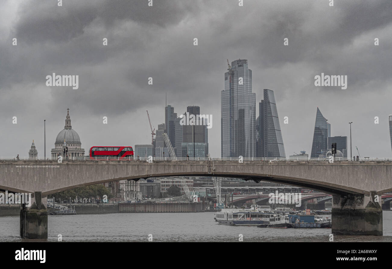 Waterloo Bridge sul fiume Tamigi su un livello di grigio nebbioso giorno con un rosso double decker bus londinese passando sopra. St Pauls, e la città di Londra buildi office Foto Stock