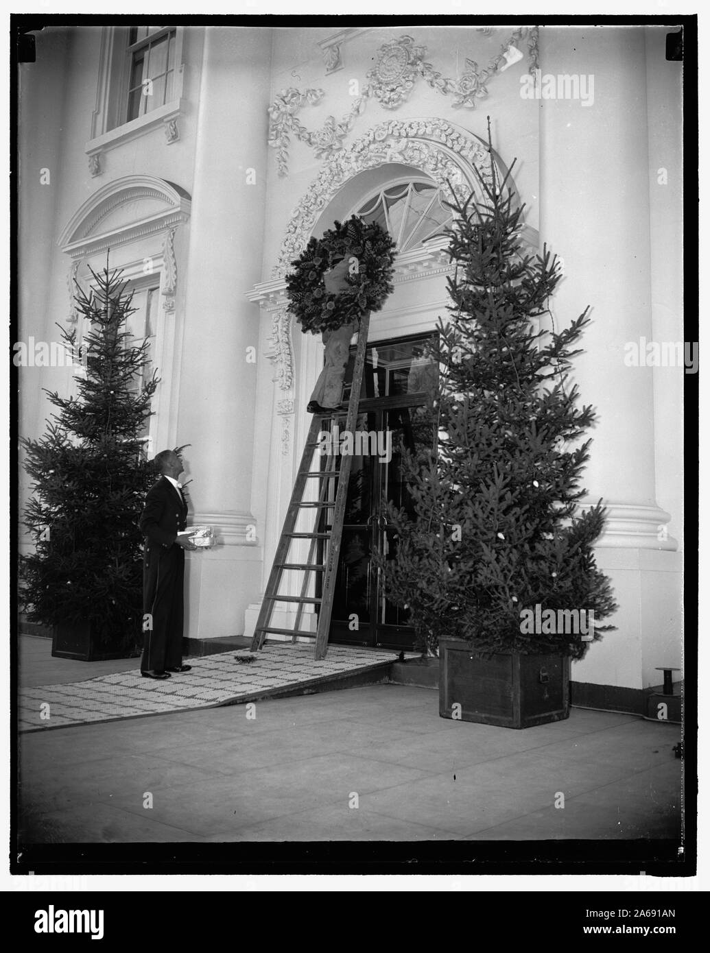 Lo spirito di natale in aria alla Casa Bianca. Washington D.C., Dic 21. Operai posizionando una ghirlanda di Natale sopra la porta della Casa Bianca di oggi. Gayly colorate luci elettriche sono state installate sugli alberi sulla parte anteriore portico, 12/21/37 Foto Stock