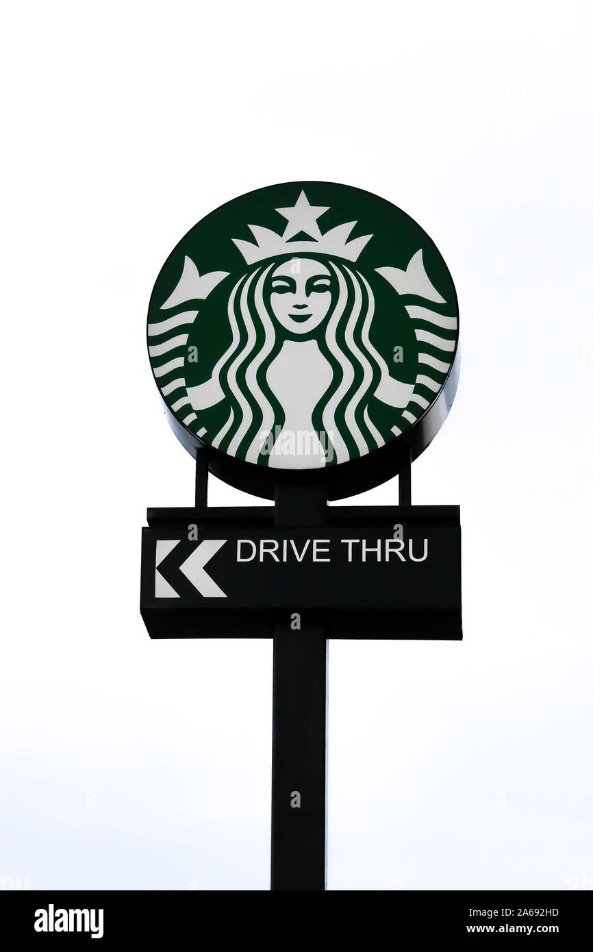 Un segno esterno contro un cielo grigio Sfondo per uno Starbucks Drive Thru con il logo di Starbucks al di sopra del Drive Thru. Foto Stock