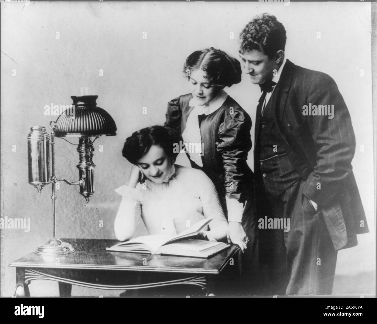 Le giovani donne e il giovane uomo la lettura con la luce di una lampada brevettata Foto Stock