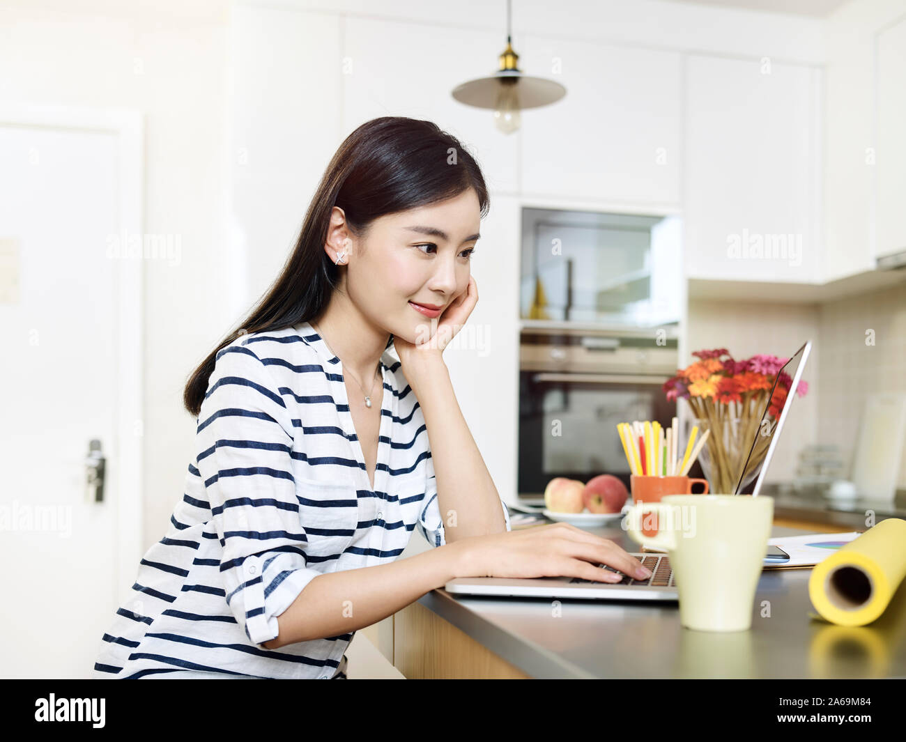 Bella giovane donna asiatica che lavorano da casa seduti al bancone cucina utilizzando il computer portatile Foto Stock