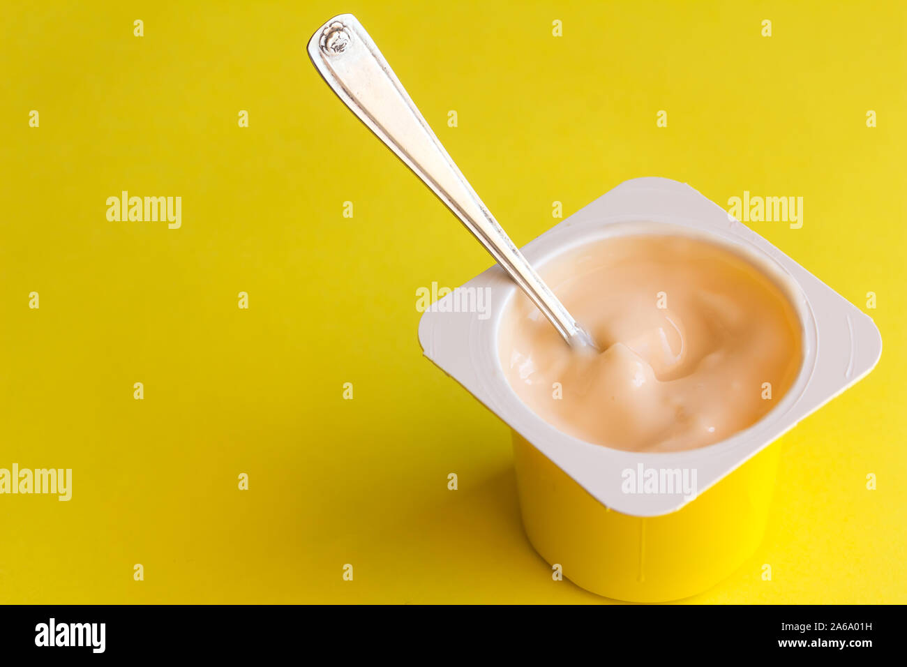 Il yogurt in contenitore di plastica con piccolo cucchiaio isolato su sfondo giallo Foto Stock
