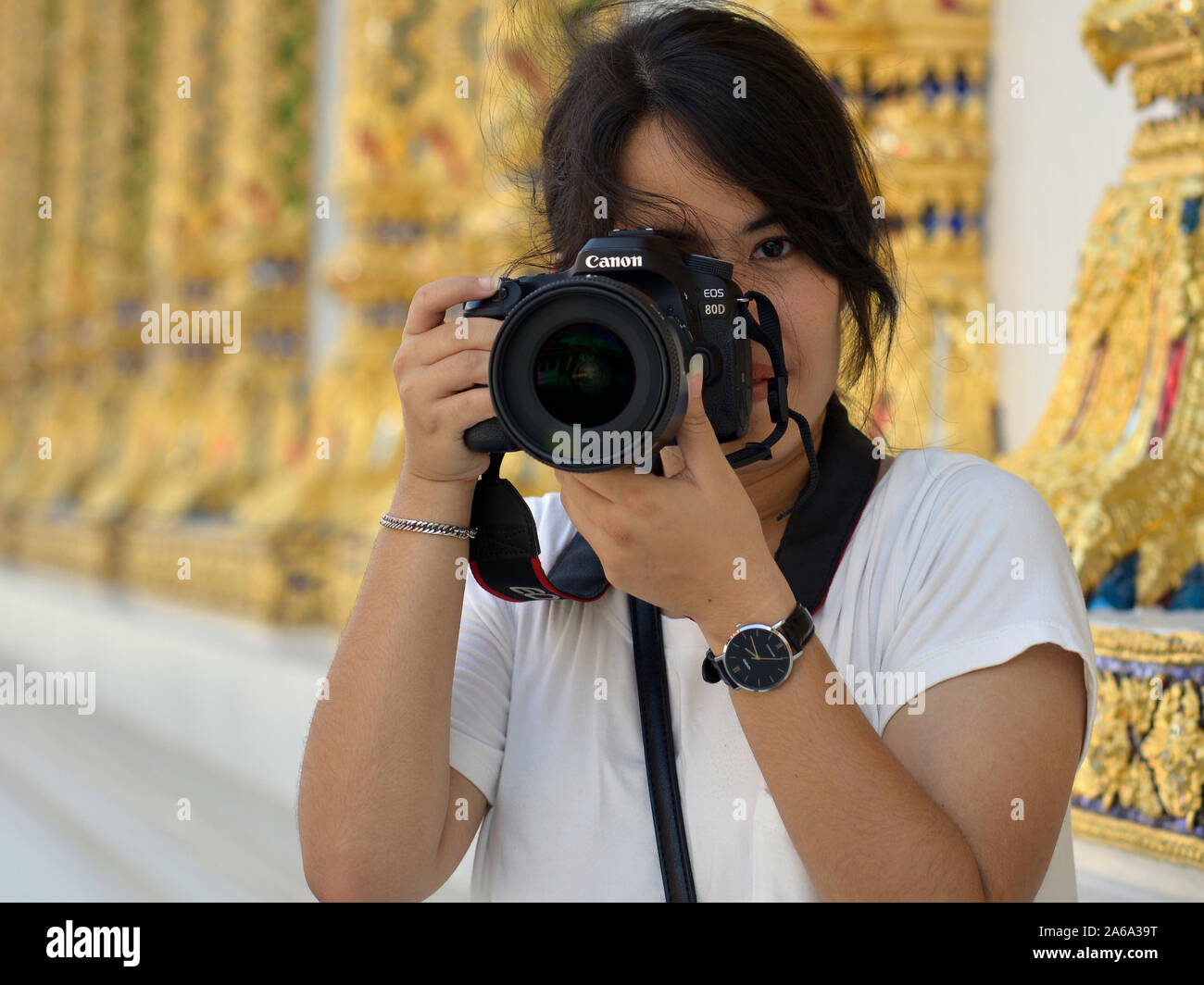 Giovani tailandesi fotografo femmina trattiene una Canon fotocamera reflex digitale EOS 80D con entrambe le mani di fronte a Bangkok il Wat Chana Songkhram Ratchaworawihan. Foto Stock