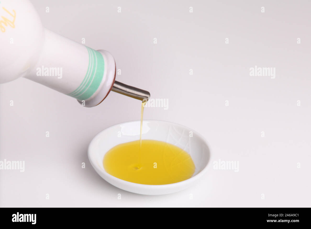 Versando l'olio di oliva in un piccolo piatto bianco isolato sopra sfondo bianco con spazio per la copia Foto Stock