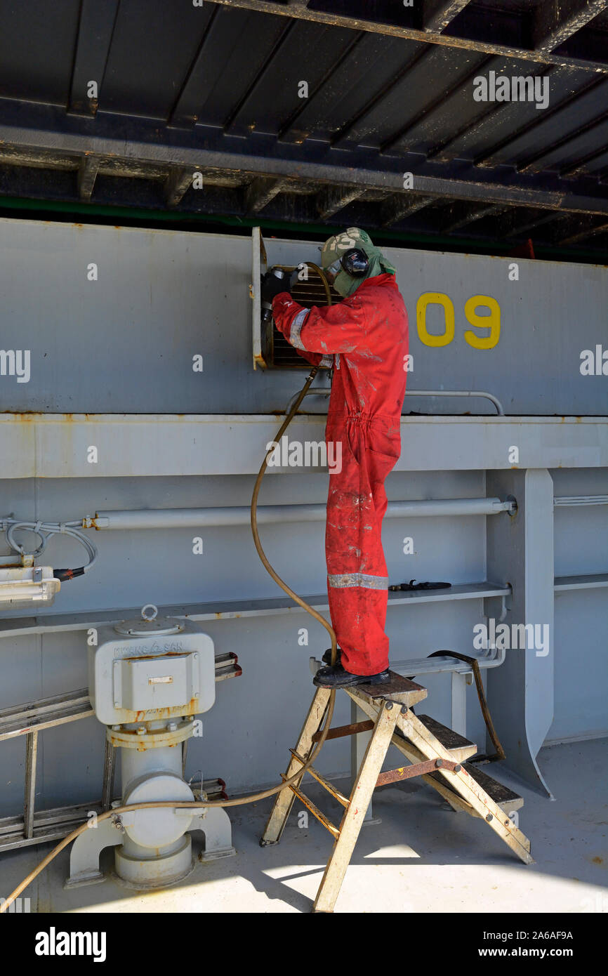 Oceano indiano, international - 2015.11.25: un marinaio filippino rimuovere la ruggine da una stiva aletta di ventilazione sul ponte principale della vigilia di container Foto Stock