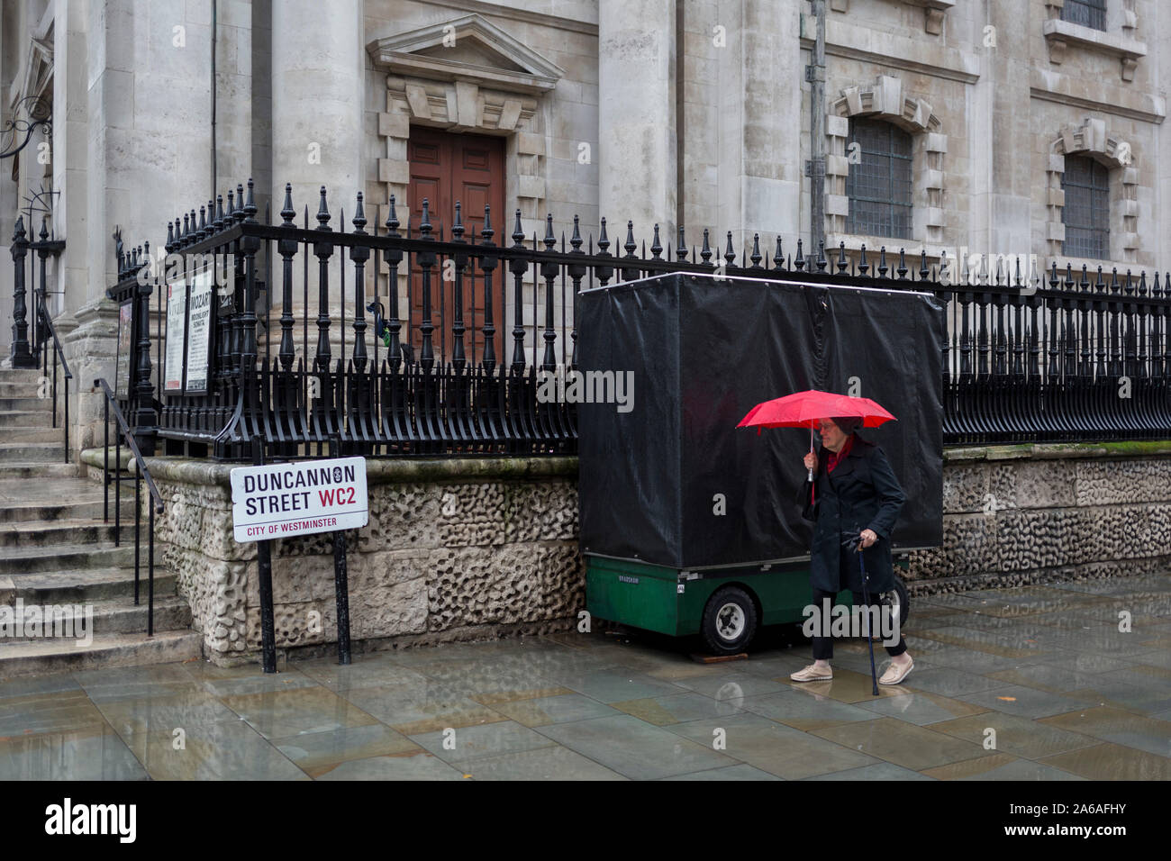Una signora anziana resiste a pioggia pesante in un pomeriggio autunnale al di fuori di San Martin-in-the-Fields Church su Duncannon Street WC2, il 24 ottobre 2019, in Westminster, Londra, Inghilterra. Foto Stock