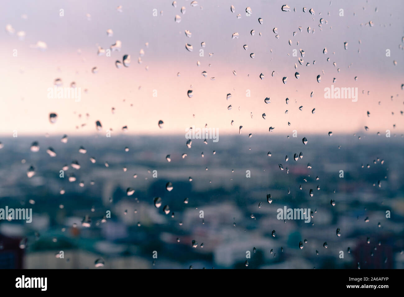 Gocce di pioggia sulla finestra appartamento con vivaci città tramonto sfondo sfocato - le goccioline di acqua sul grattacielo piano di vetro con urban golden ora sky - Meteo, umore e il concetto di stagione Foto Stock