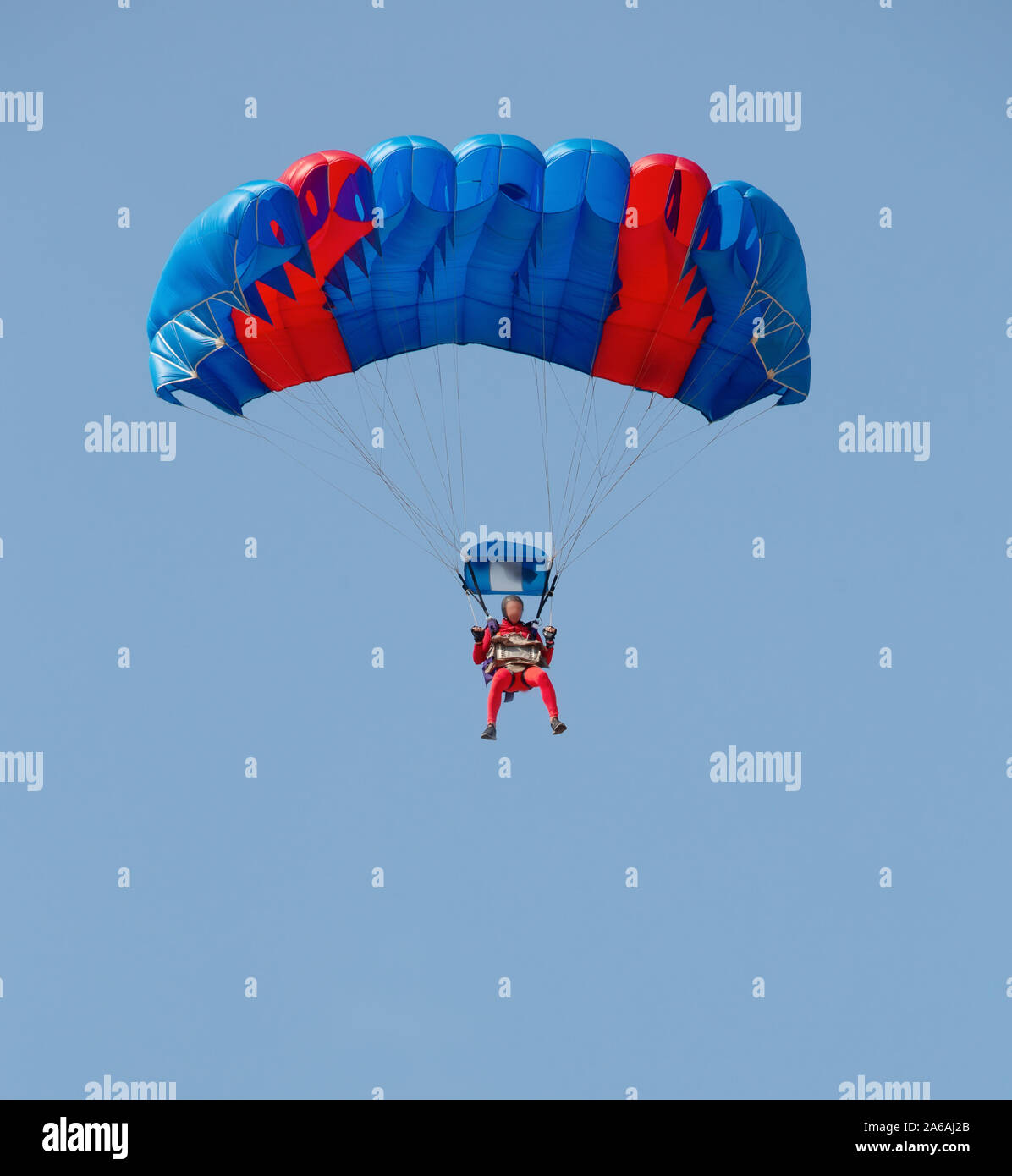 Il rosso e il blu paracadute con un paracadutista nel cielo. Il volto è vago e irriconoscibile Foto Stock