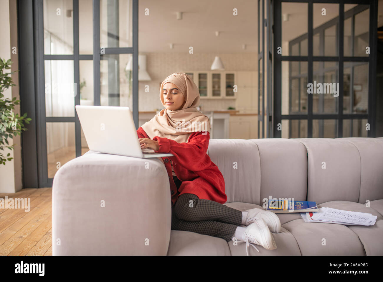 Ragazza giovane seduto comodamente sul divano mentre si lavora sul suo computer portatile Foto Stock