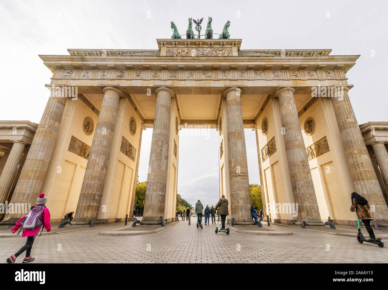 Il traffico di persone a piedi o in scooter elettrico sotto il soleggiato Porta di Brandeburgo, Berlino, Germania Foto Stock