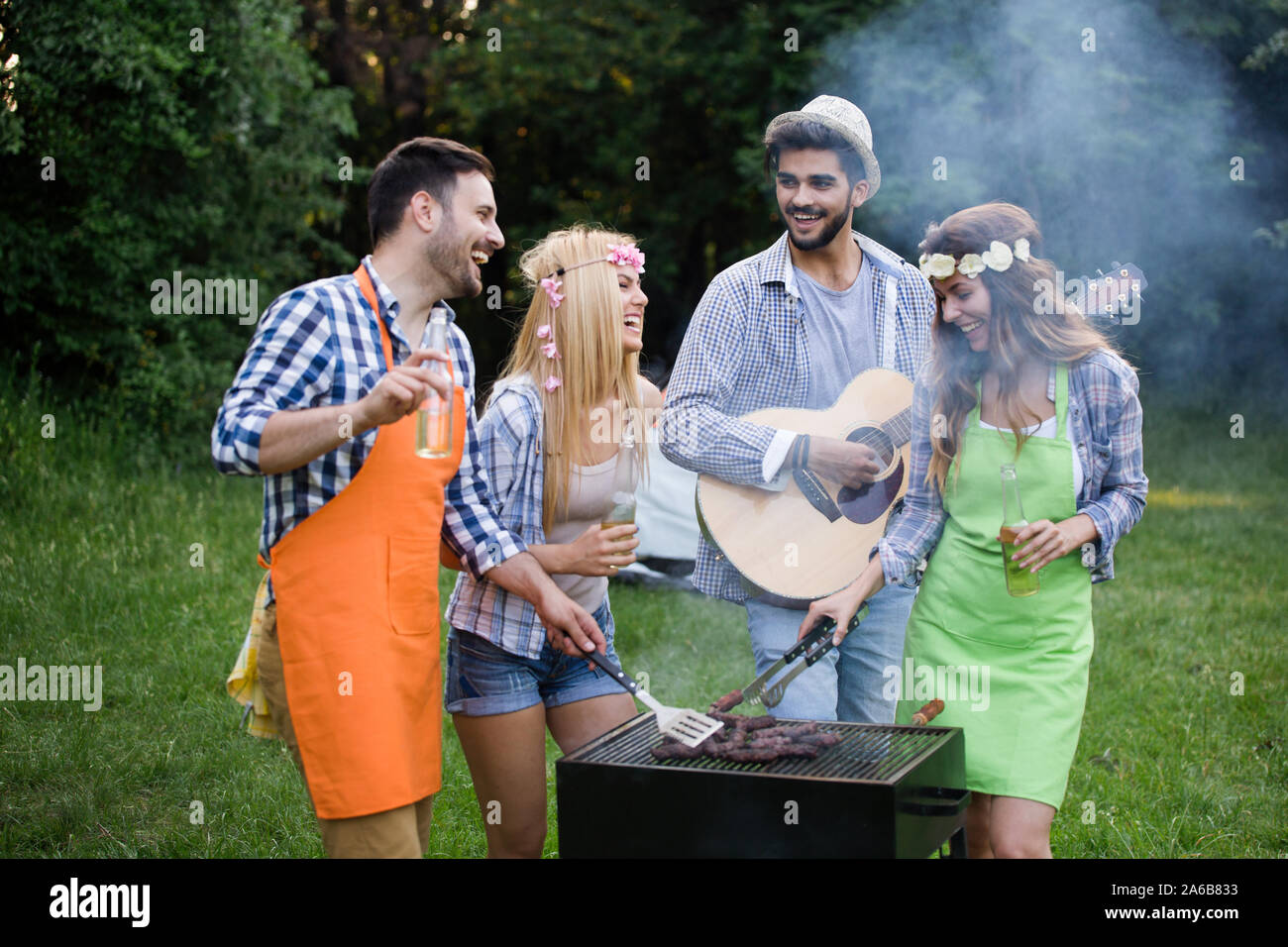 Gruppo di persone felici intorno permanente grill, chat, bere e mangiare. Foto Stock