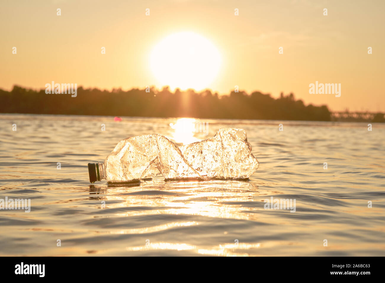 Crumpled trasparente bottiglia di plastica galleggia sulla superficie dell'acqua. Sunset, il verde degli alberi. Persone e di ecologia. Riverside inquinamento. La conservazione del Foto Stock