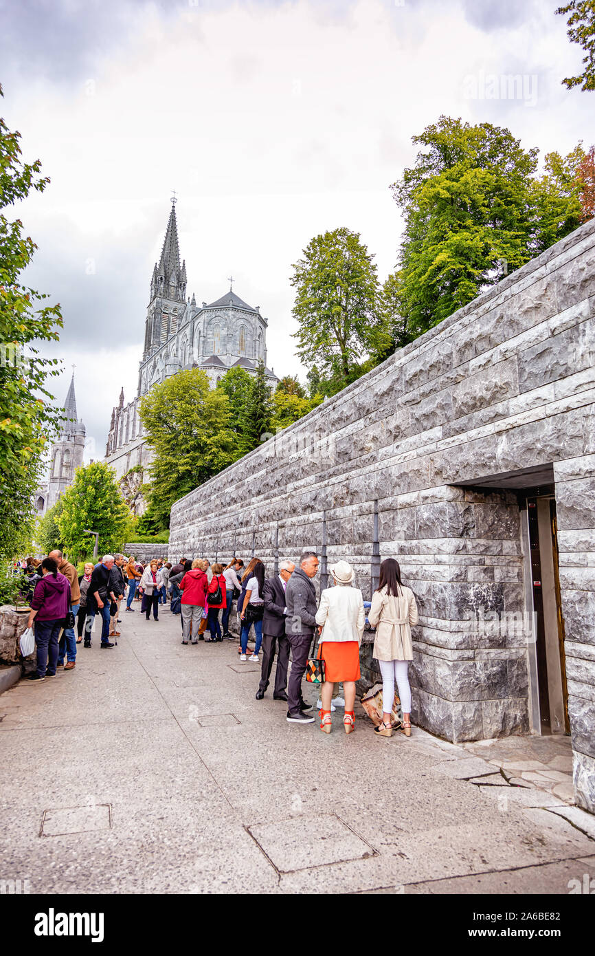 LOURDES - Giugno 15, 2019: Vista di fedeli il riempimento di bottiglie di acqua santa vicino alla grotta e la cattedrale di Lourdes Foto Stock
