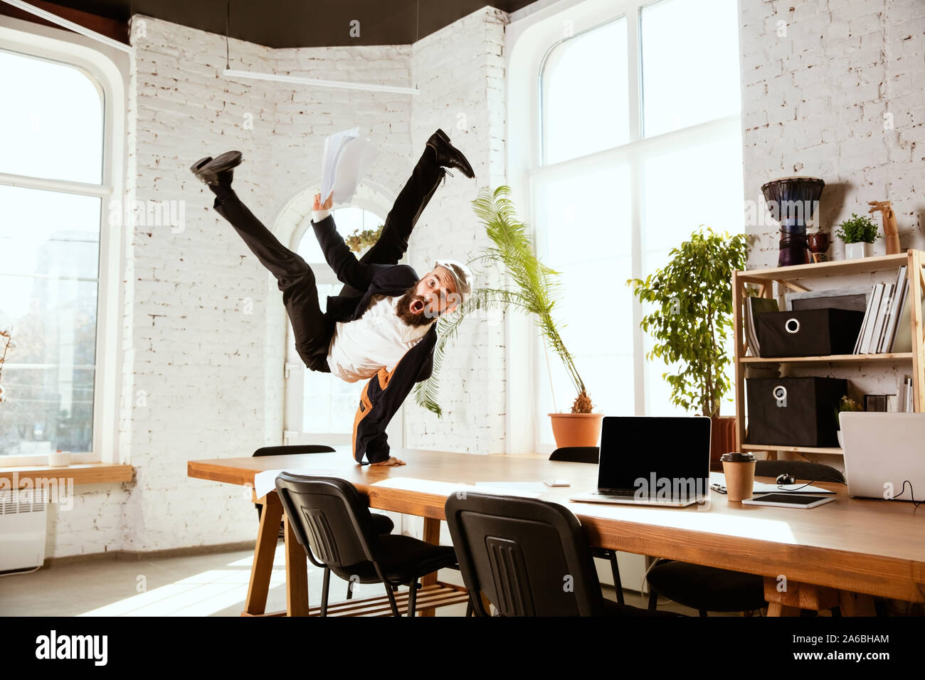 Giovane imprenditore caucasico divertirsi ballare break dance in ufficio moderno al tempo di lavoro con i gadget. Gestione, libertà, attività professionale, un modo alternativo di lavorare. Ama il suo lavoro. Foto Stock