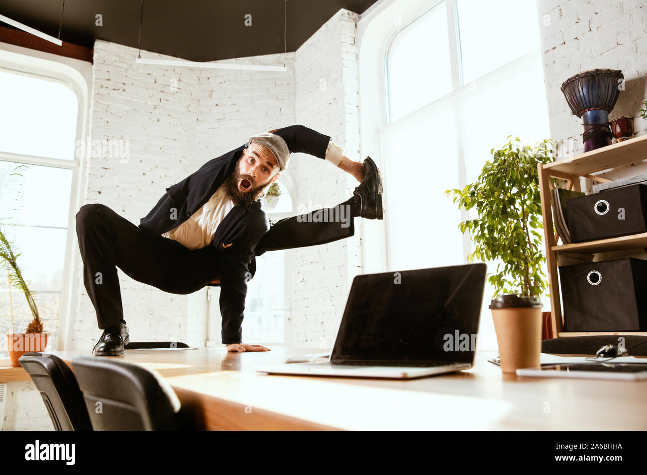Giovane imprenditore caucasico divertirsi ballare break dance in ufficio moderno al tempo di lavoro con i gadget. Gestione, libertà, attività professionale, un modo alternativo di lavorare. Ama il suo lavoro. Foto Stock