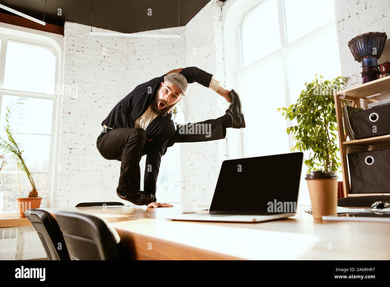 Giovane imprenditore caucasico divertirsi ballare break dance in ufficio moderno al tempo di lavoro con i gadget. Gestione, libertà, attività professionale, un modo alternativo di lavorare. Ama il suo lavoro. Foto Stock