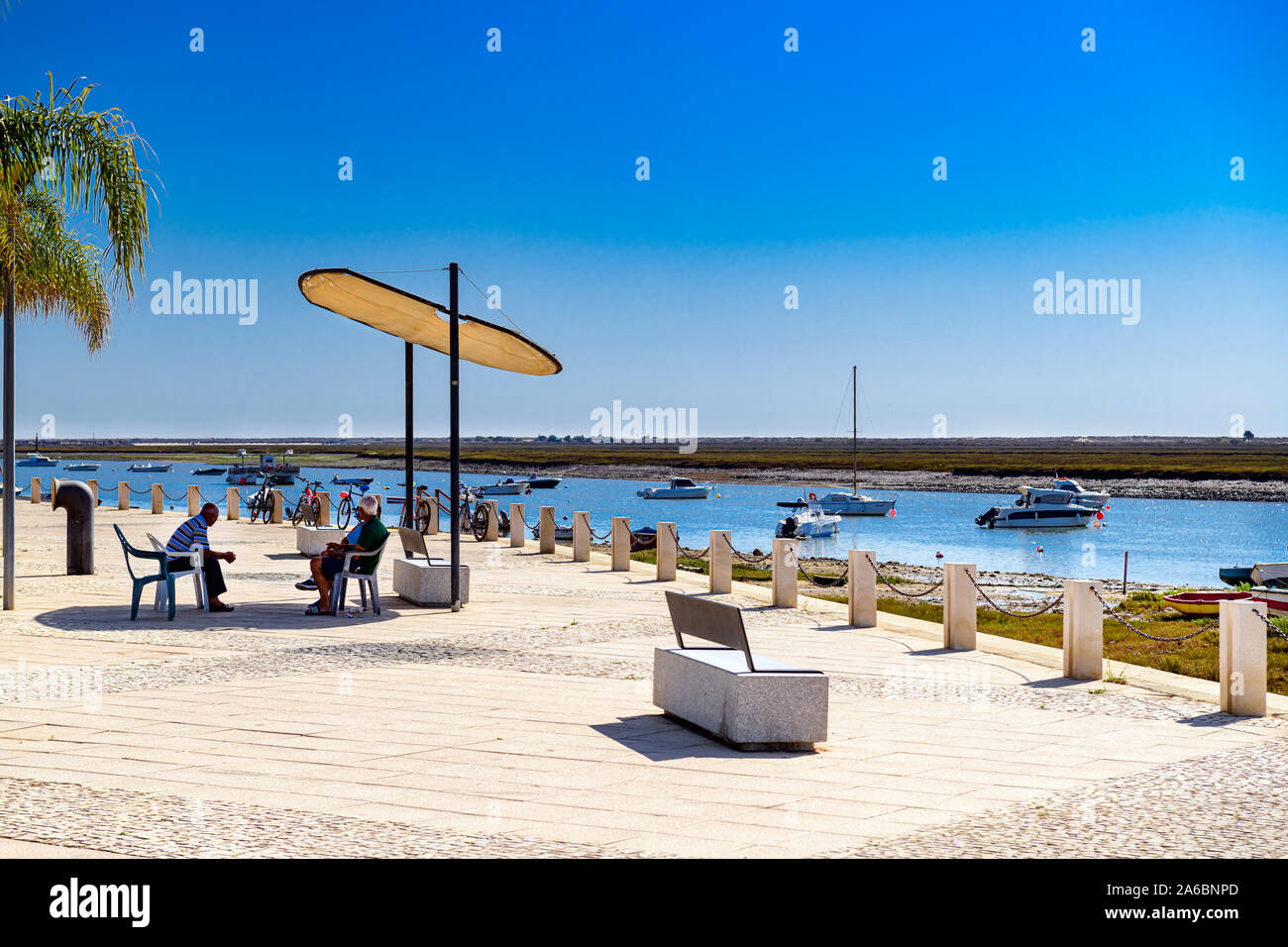 Passeggiata Santa Luzia accanto a Ria Formosa con panchine e ombrelloni. Il litorale ha la pesca e le barche da diporto Santa Luzia. Algarve, Portogallo. Foto Stock