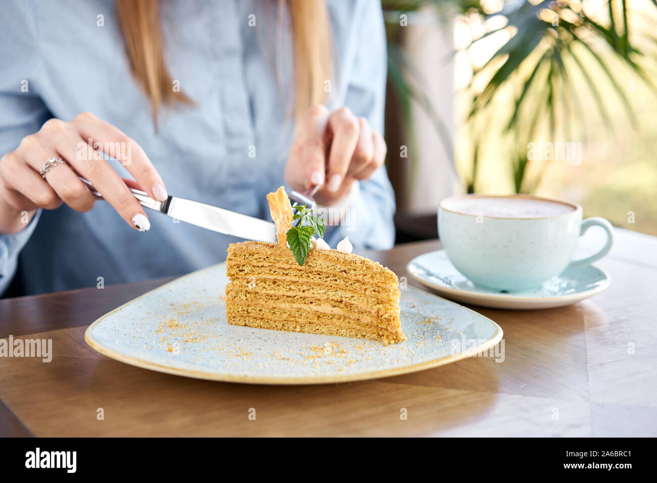 Il miele di pan di spagna decorata con meringa e foglie di menta. Una giovane donna beve caffè cappuccino in un ristorante e mangia il dessert. Prima colazione in Foto Stock