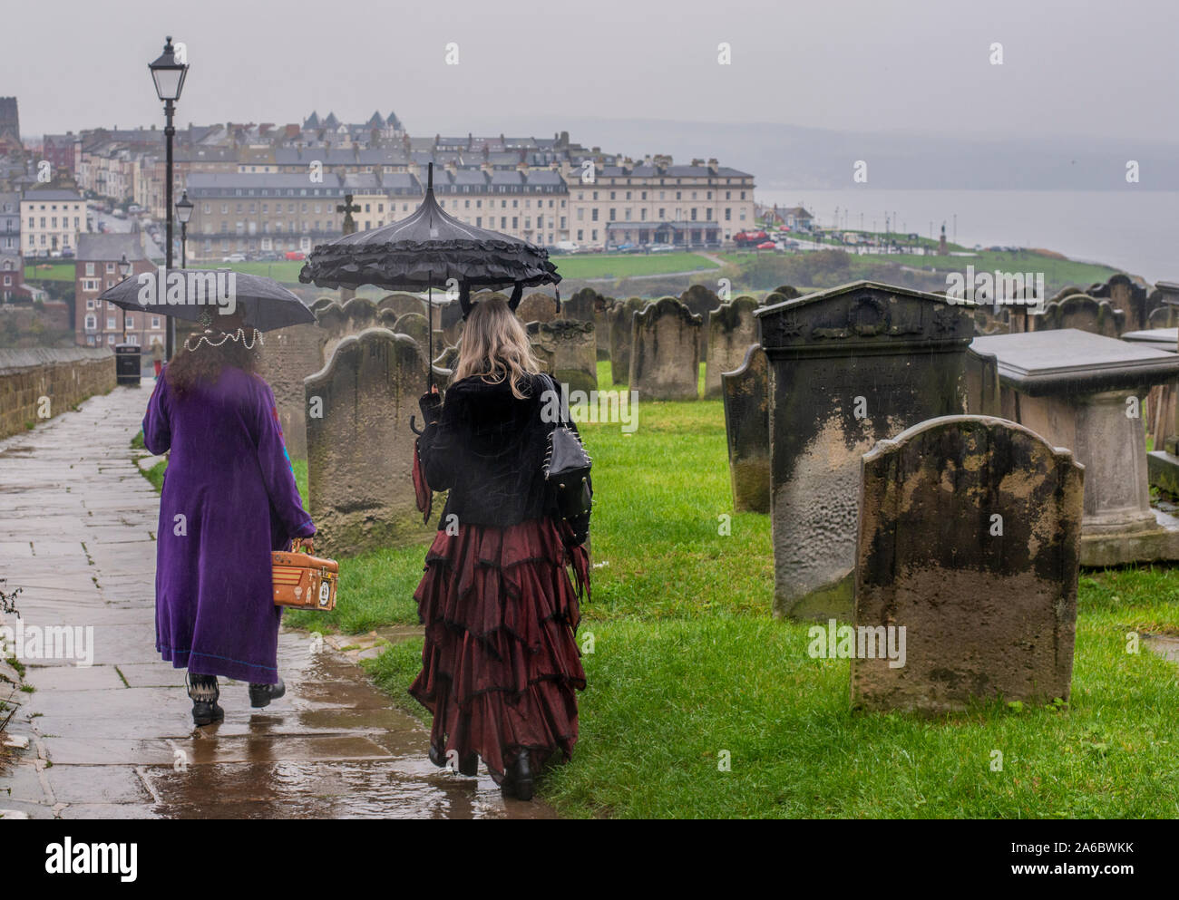 Due donne nei tradizionali costumi di Goth a piedi sotto la pioggia per la città, Whitby Goth Festival Weekend, Whitby, North Yorkshire, Regno Unito, 25 Ottobre 2019 Foto Stock