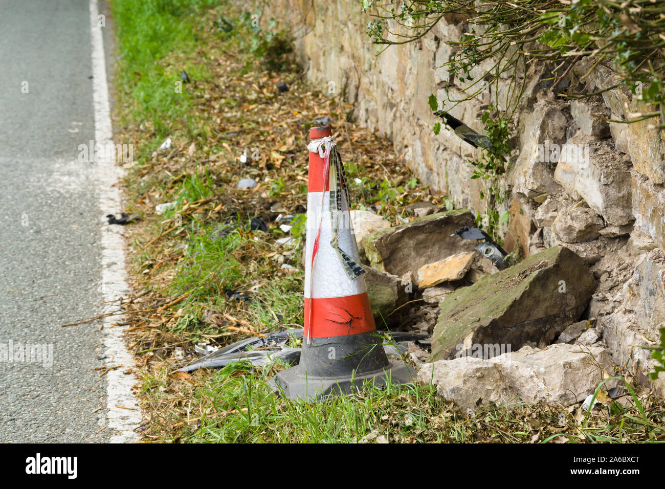 Avanzi di purè di pezzi di rottami i detriti di un cono di plastica e nastro a sinistra su una corsia rurale vettura dopo un urto con un muro di pietra nel Regno Unito Foto Stock