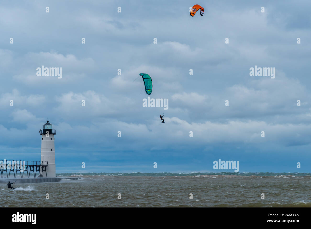 Un kite surfer vola in alto nella parte anteriore del Manistee North Pierhead Lighthouse in Michigan, USA con un altro kite surfer è sulla superficie dell'acqua. Foto Stock