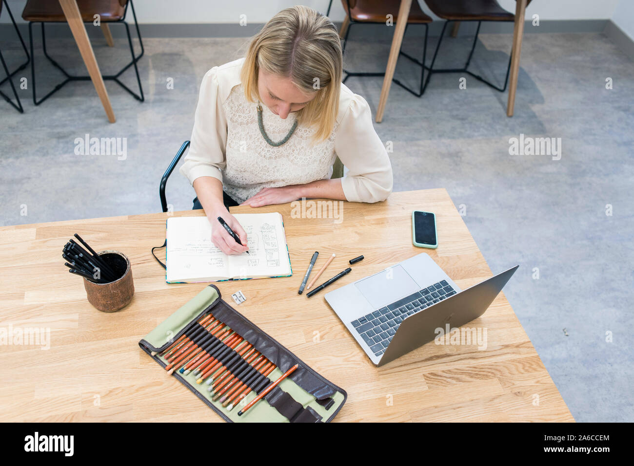 Una donna si siede a un tavolo in un cafe rendendo note e schizzi in un blocco note Foto Stock
