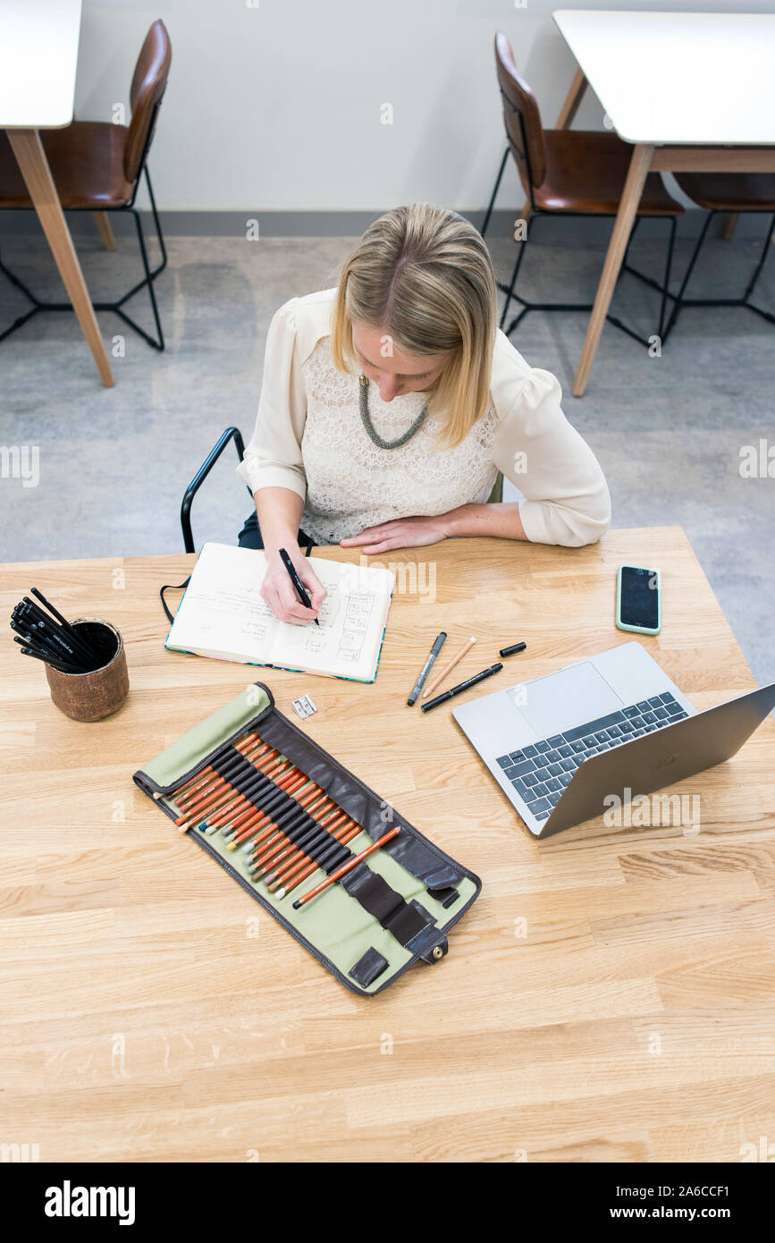 Una donna si siede a un tavolo in un cafe rendendo note e schizzi in un blocco note Foto Stock