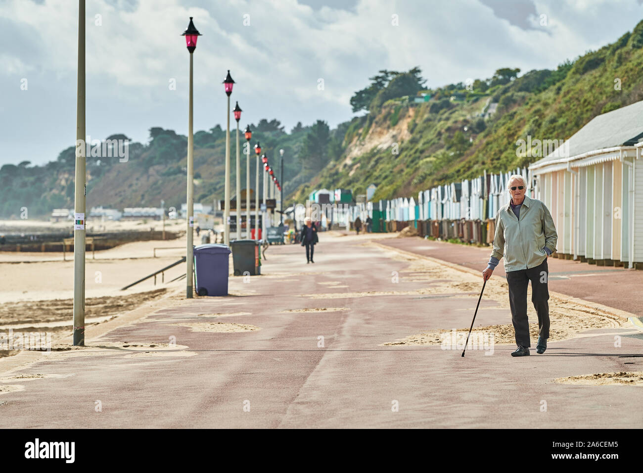 Un uomo anziano con il suo camminare sitck passeggiate sul lungomare a fianco di cabine sulla spiaggia, accanto alla spiaggia di sabbia a Bournemouth, Inghilterra. Foto Stock