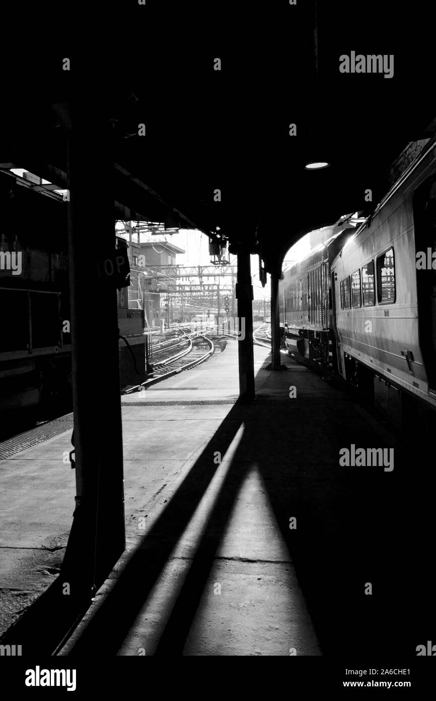 Drammatico pomeriggio luce alla Hoboken terminal del treno. Luce posteriore di creare forti ombre su tutta la piattaforma, treno e tracce. Verticale B/W photog Foto Stock