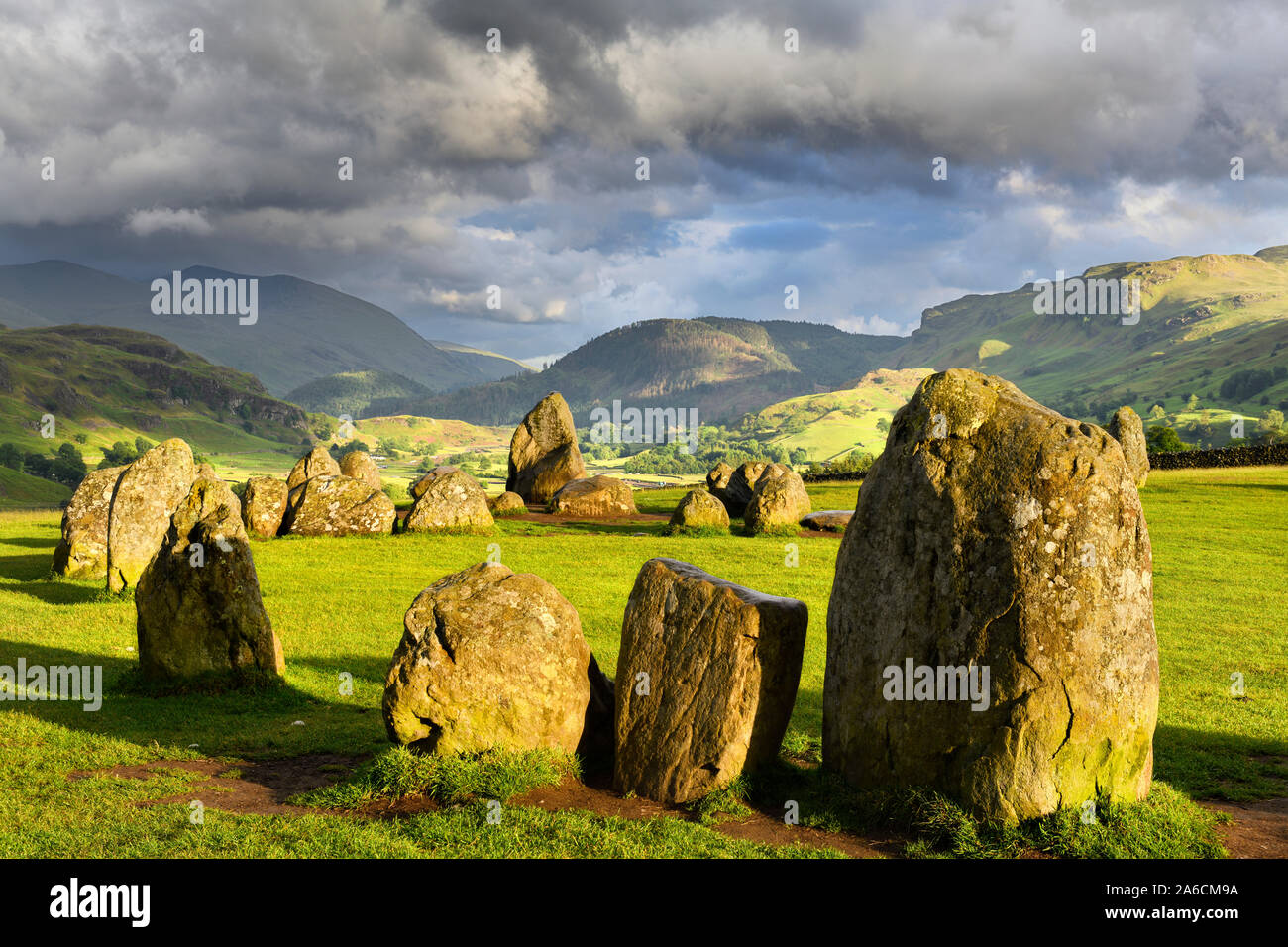 Sun su Castlerigg Stone Circle sotto le nuvole scure solstizio d'estate vigilia con Naddle villaggio nei monti Pennini Lake District Inghilterra Keswick Foto Stock