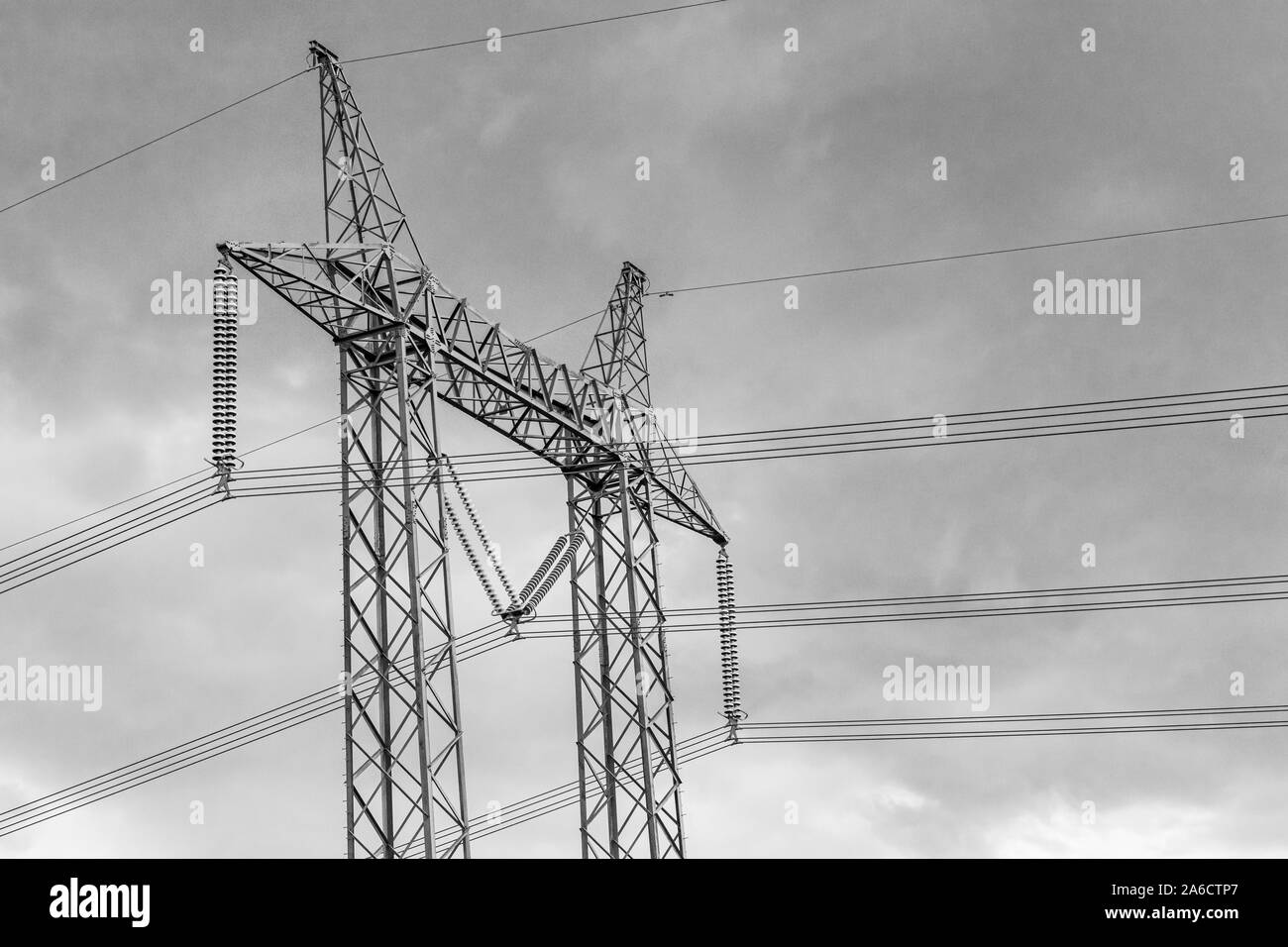 Un basso angolata e visualizzazione bianco e nero di un pilone elettrico, travatura reticolare in acciaio del telaio di supporto della torre di energia elettrica ad alta tensione con cavi camera per tipo. Foto Stock