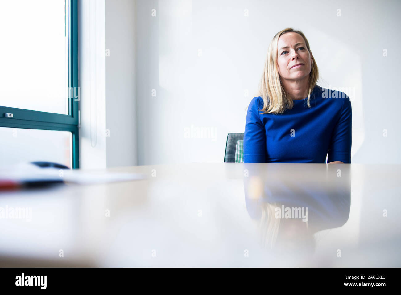 Una donna bianca si siede attorno a un tavolo per riunioni in un luminoso ufficio con un sacco di windows in una smart suit Foto Stock
