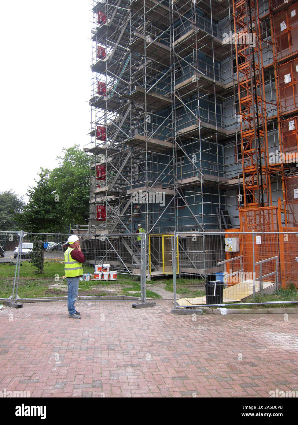 Ottobre 2013 - uomo in piedi accanto a un blocco di appartamenti che è coperta da impalcature Foto Stock