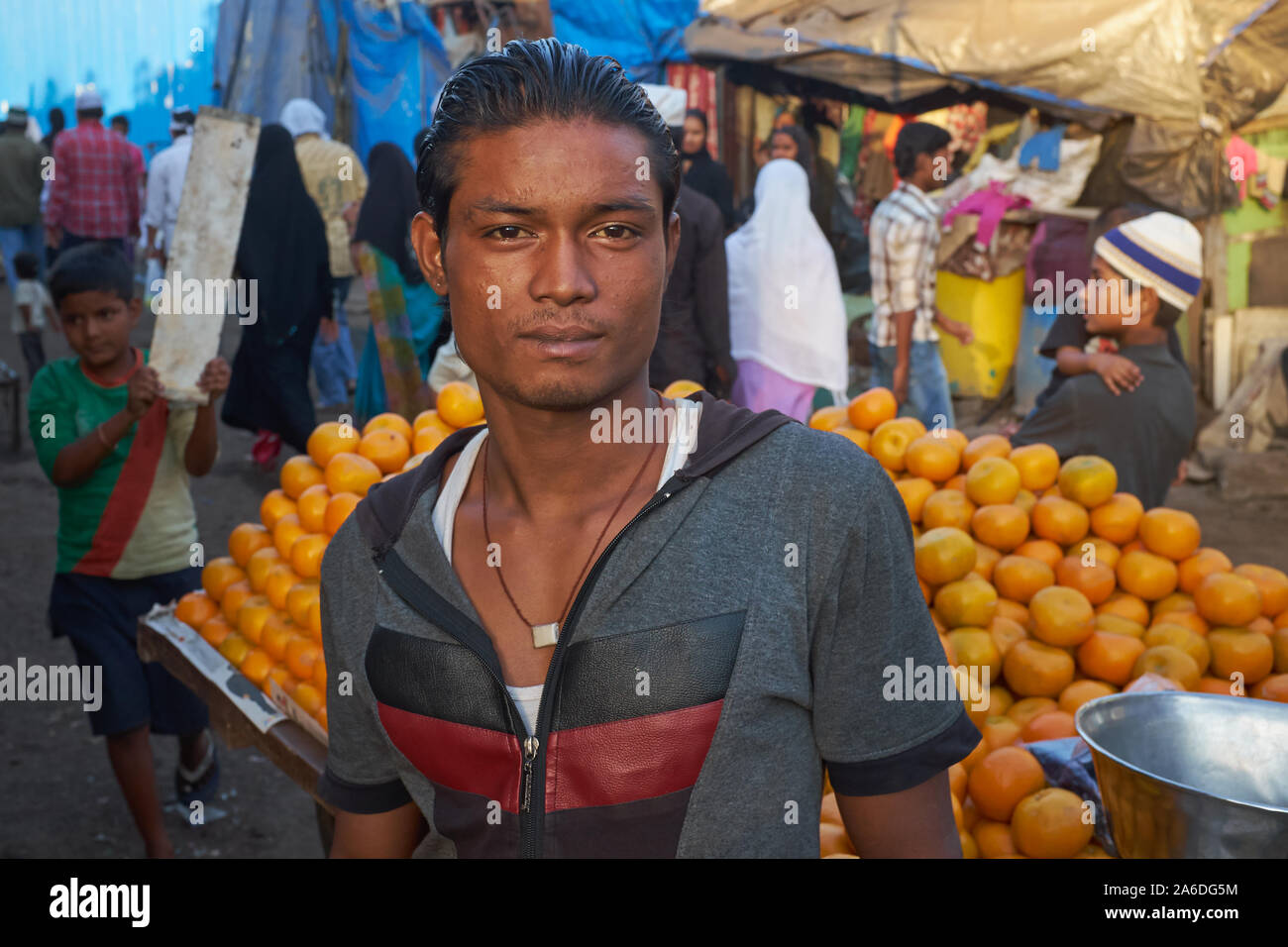 Un uomo in Darukhana delle baraccopoli di Mumbai, India, pone di fronte a un carrello carico di arance Foto Stock