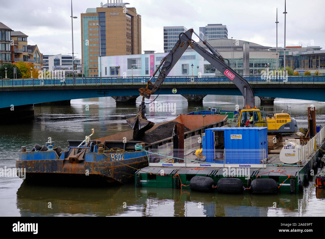 Chiatta dragaggio facendo lavorare sul fiume Lagan con digger il trasferimento di sporcizia dalla chiatta più piccoli Foto Stock