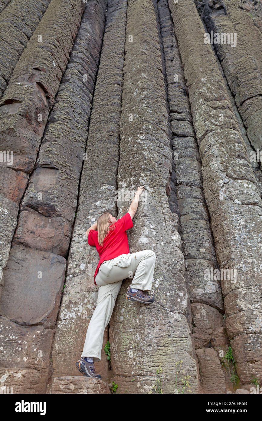Una donna finge di salire le colonne di basalto al Giants Causeway nella contea di Antrim, Irlanda del Nord. Foto Stock